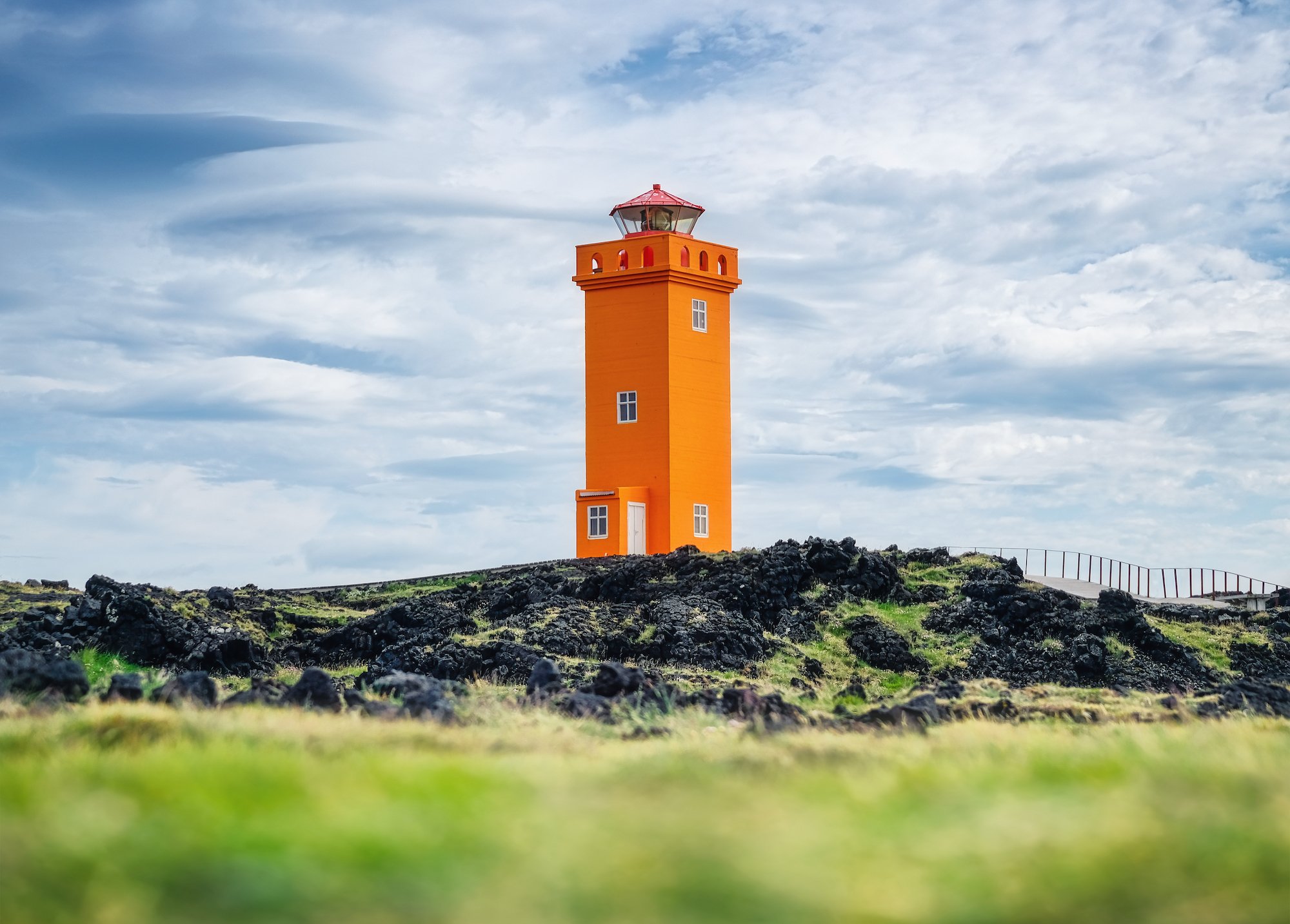 Un faro arancione brillante si erge su un paesaggio erboso e roccioso sotto un cielo nuvoloso