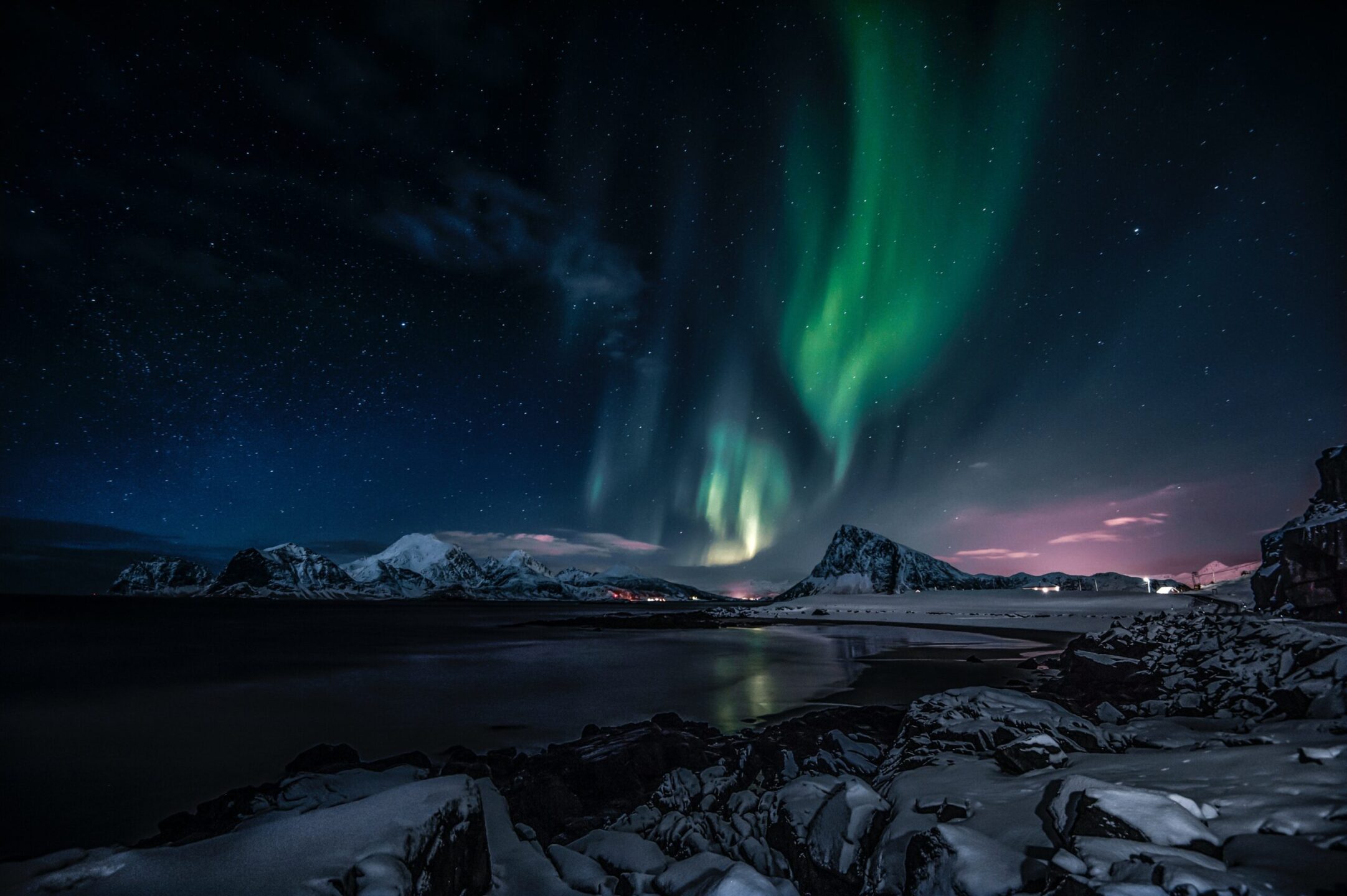 L’esperienza dell’aurora boreale su una costa innevata, con montagne che si stagliano contro un cielo stellato