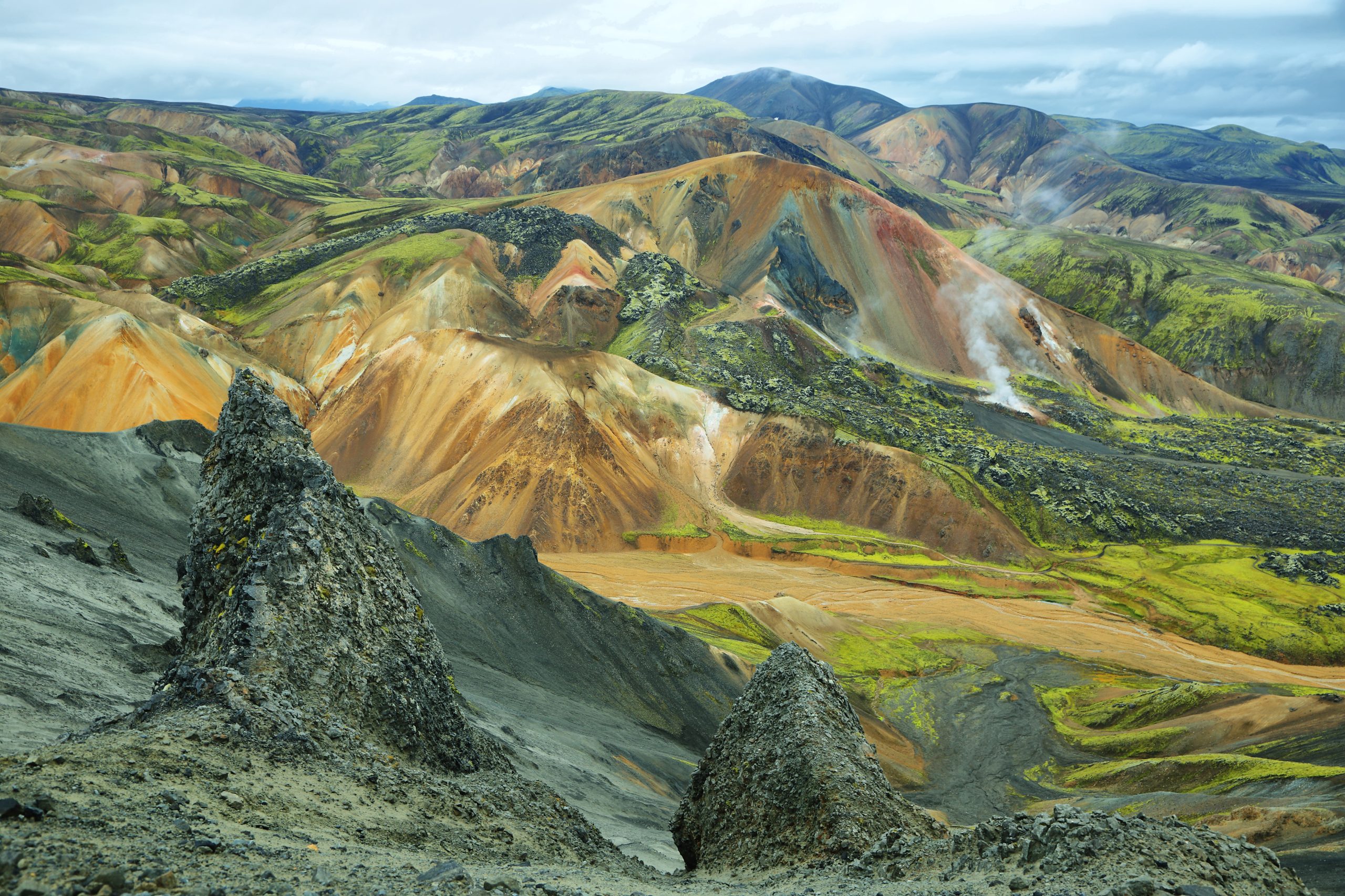 Vista delle colorate montagne di riolite e delle sorgenti di vapore a Landmannalaugar,, con uno sfondo roccioso e un cielo nuvoloso